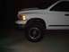 2001 Dodge 1500 - Front corner of a white 2001 Dodge 1500 pickup truck, showing the headlight, grille, and wheel.