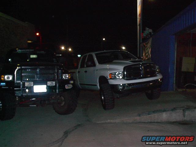 Front view of a black Dodge Ram and a white Dodge Ram parked at night