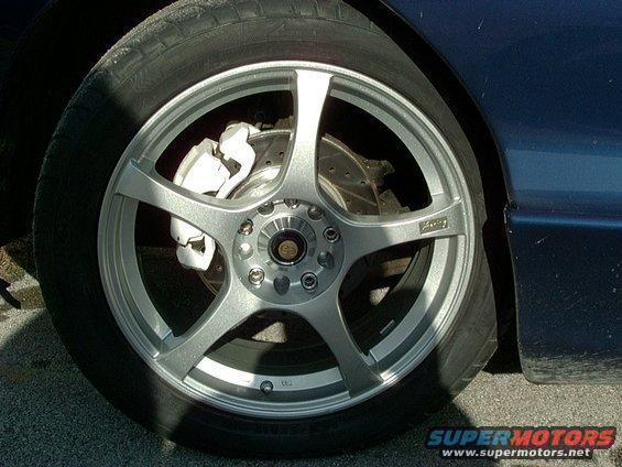 Silver five-spoke aftermarket wheel with white brake caliper on a dark blue car