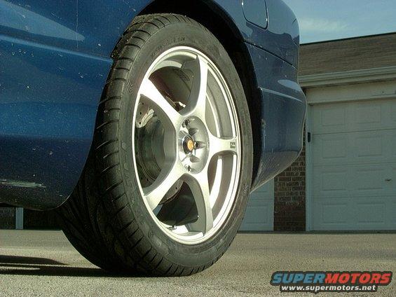 Blue car rear quarter panel and alloy wheel with tire. Garage door in background