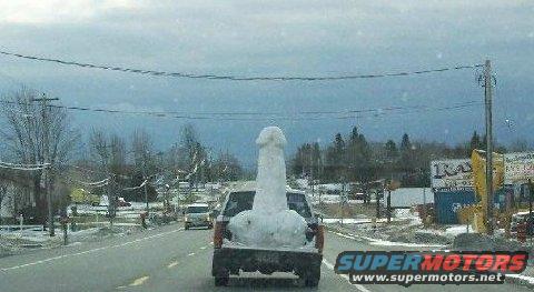 Pickup truck with a snow sculpture in its bed, driving on a snowy road