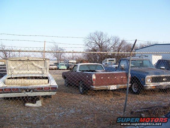 Brown Ford Ranchero with a white top, seen from the rear in a junkyard