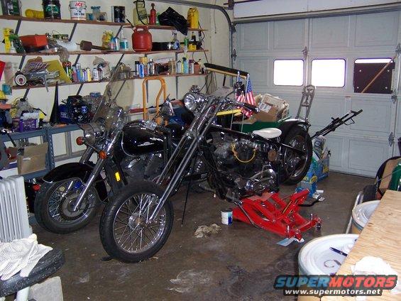 Two motorcycles, one black cruiser and a chopper, parked in a cluttered garage