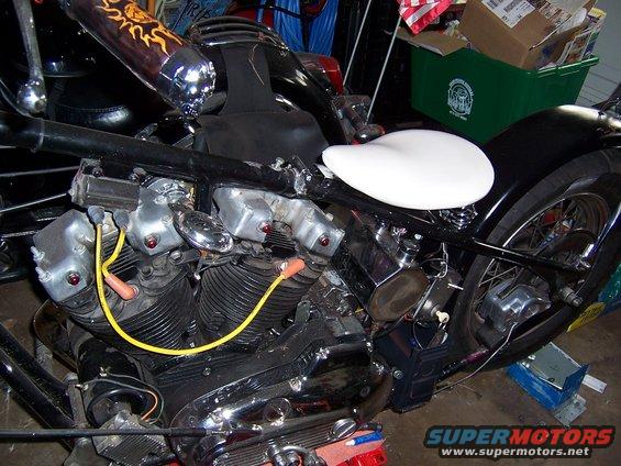 Close-up of a motorcycle's V-twin engine with yellow spark plug wires and a white seat