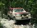 1995 Ford Bronco - A muddy Ford Bronco navigates a rocky path through a dense forest.