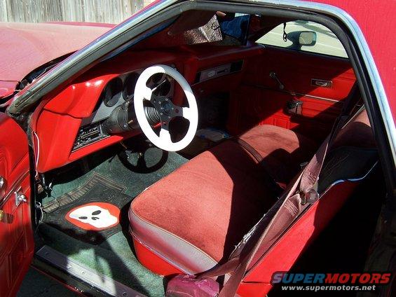 Red car interior with white steering wheel, red seats, and a ghost-shaped floor mat