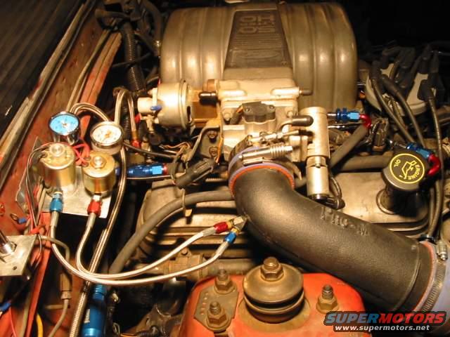 Engine bay with multiple gauges and hoses connected to engine components. Includes oil cap with engine symbol