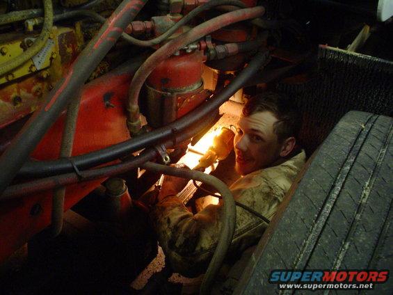 Mechanic works on engine with a flashlight. Tire visible