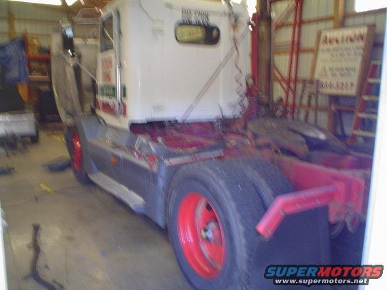 Semi-truck tractor with red wheels in a garage. Auction sign in background