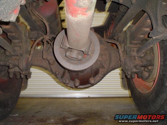 Underside view of a vehicle's rear axle and driveshaft assembly. Shows differential housing, U-joint, and suspension components