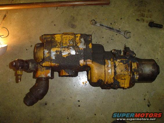 Yellow and black hydraulic pump with peeling paint, on a concrete floor with tools