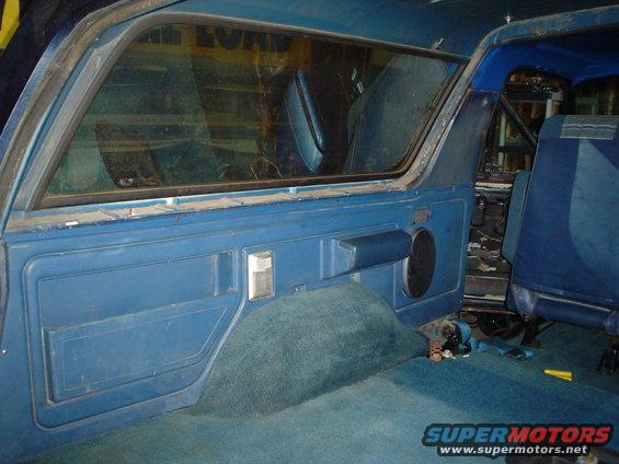 Interior shot of a blue vehicle, showing the door panel, rear seat, and carpet. Some parts appear to be removed