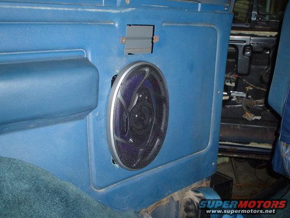 Blue interior door panel with a round speaker installed. Wires are visible behind the panel