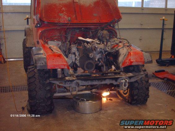 Red Jeep with hood open, engine exposed, in a garage. Large off-road tires visible