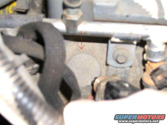 Close-up of engine components with a red arrow pointing to a circular metal cap