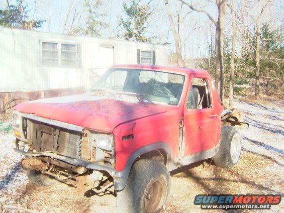 Red Ford Bronco with front end damage and missing doors, parked in a yard