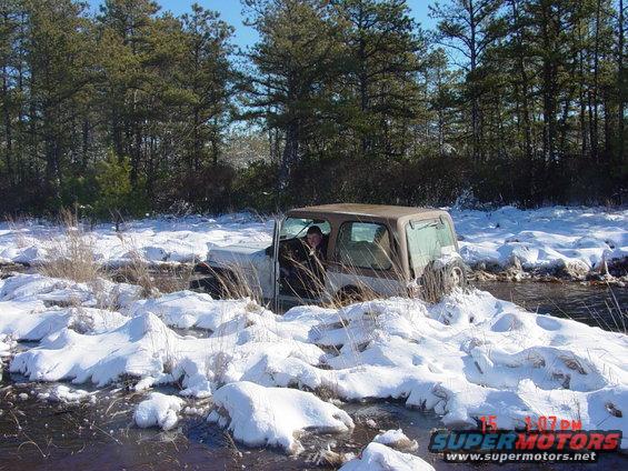 Brown Jeep Wrangler stuck in snow and water, driver visible