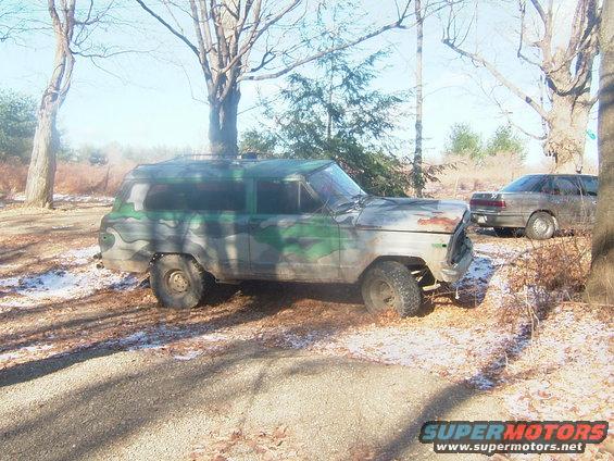 Camouflaged SUV with rust on the hood, parked outdoors with another car behind it