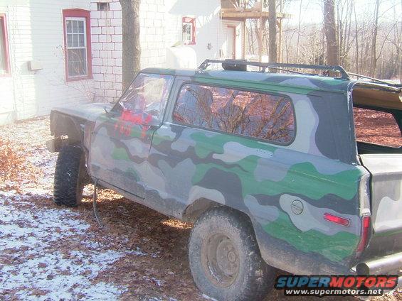 Camouflaged SUV with roof rack parked in a yard with snow on the ground