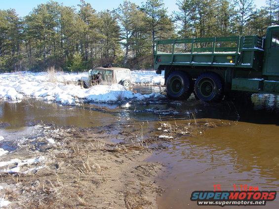 Jeep stuck in water and snow, with a large green military truck nearby