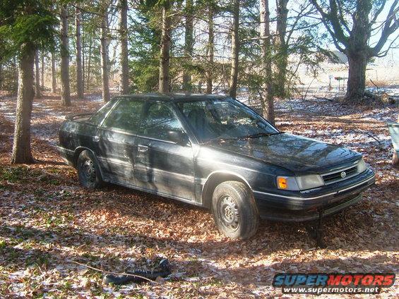 Black sedan with a prominent grille and headlights, parked in a wooded area