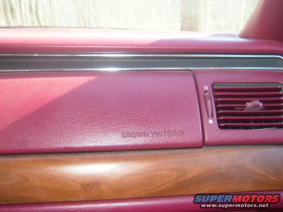 Dashboard of a car with 'CROWN VICTORIA' embossed on the dash, wood trim, and a red interior