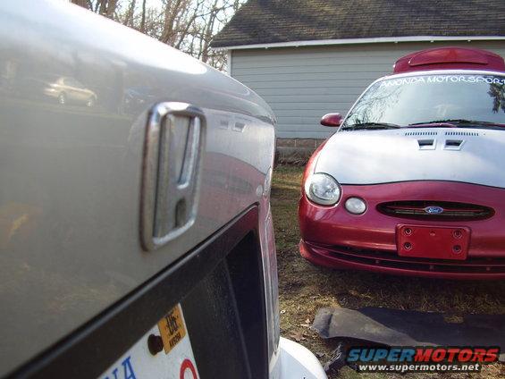 Close-up of Honda emblem on car; red Ford Taurus in background
