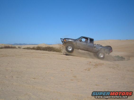 Gray Ford Ranger jumping a sand dune, front wheels off the ground, aftermarket bumper