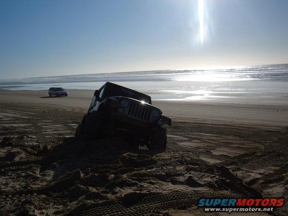 Jeep stuck in sand on beach with another SUV in the distance