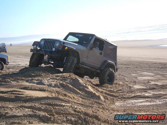 Gray Jeep Wrangler TJ climbing sand dune on beach
