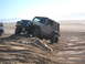 1985 Ford Ranger - A gray Jeep Wrangler TJ navigates a sandy incline on a beach, with other vehicles visible in the distance.