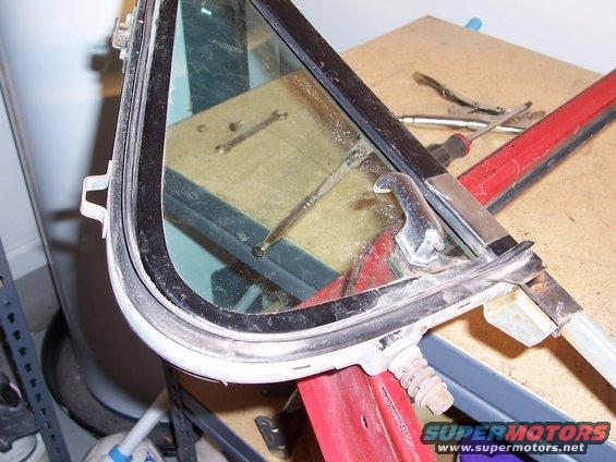Car door window frame with chrome latch and rubber seal, resting on a workbench with tools