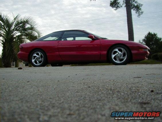 Side view of a red 1997 Ford Probe parked on pavement with palm trees and a utility pole in the background
