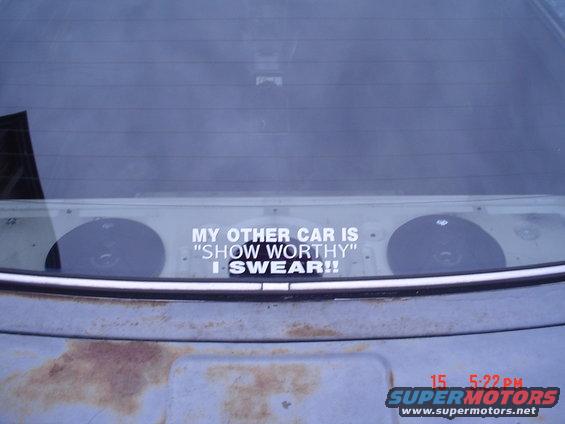 Rear window of a car with a sticker that reads 'MY OTHER CAR IS "SHOW WORTHY" I SWEAR!!' and two speakers visible