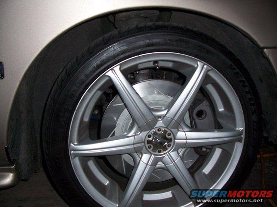 Close-up of a silver multi-spoke aftermarket wheel covering a drilled brake rotor and caliper