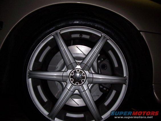 Silver alloy wheel with six spokes and a black center cap, showing brake rotor and caliper