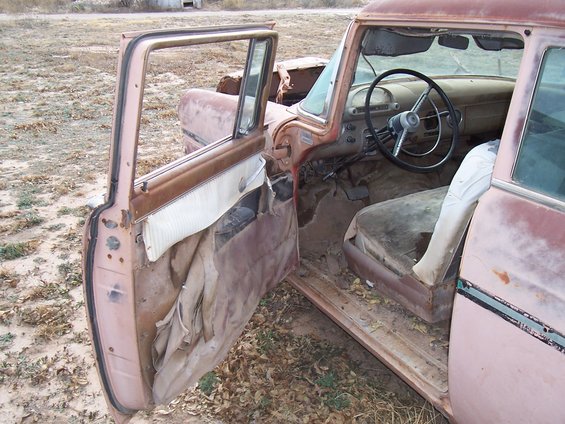 Interior of a pink 1955 Ford Customline with the driver's door open. Seats and door panels are worn