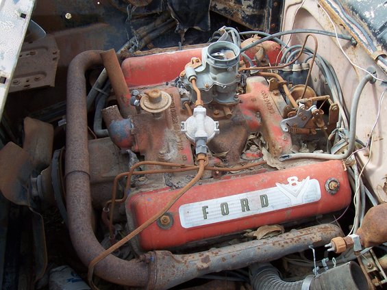 Rusty Ford V8 engine with red valve covers and a carburetor