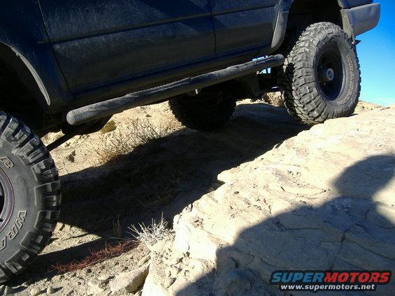Dark SUV side view with large off-road tires on rocky terrain
