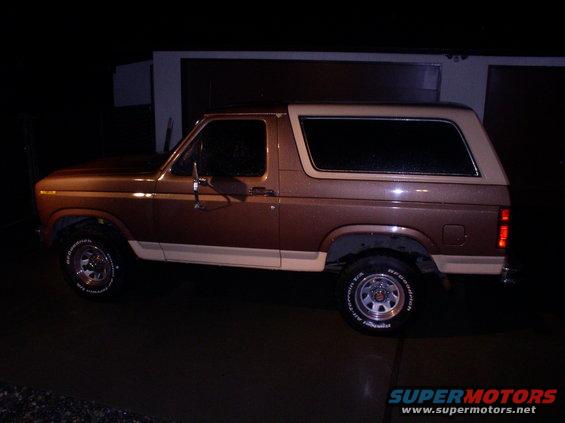 Brown and tan Ford Bronco, side view, wet surface, aftermarket wheels