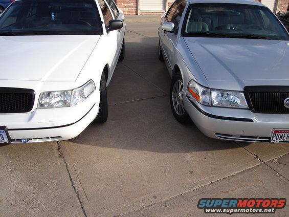 Two Ford Crown Victorias parked side-by-side, one white, one silver, viewed from the front