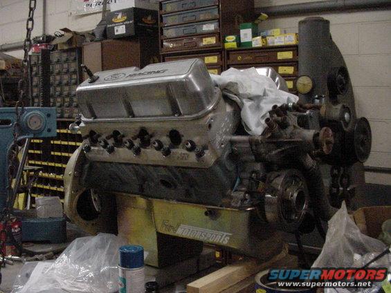 Ford Motorsports engine on stand, silver valve covers, some parts covered with white cloth