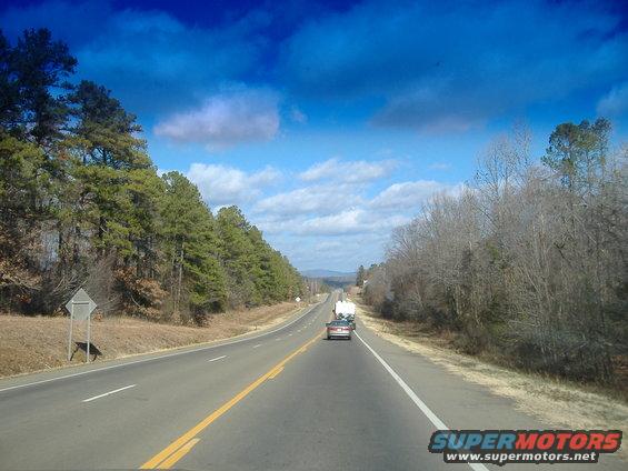 Car towing a trailer on a highway, trees and blue sky with clouds