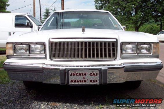 White 1988 Mercury Grand Marquis with a custom license plate that says 'Suckin Gas & Haulin Ass'