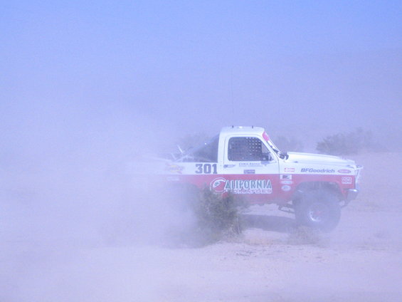 Off-road race truck kicking up dust, side view. California racing decals