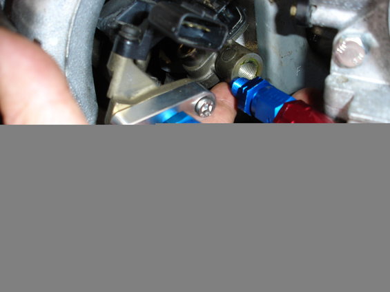 Close-up of engine components with blue and red braided hoses attached to a metal fitting