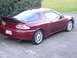 1993 Mazda MX-3 - The rear of a maroon 1993 Mazda MX-3 coupe is shown, a prominent spoiler and dual exhaust pipes.