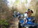 1999 Honda RANCHER - A group of ATVs are parked on a dirt trail in a wooded area, with several people around them.