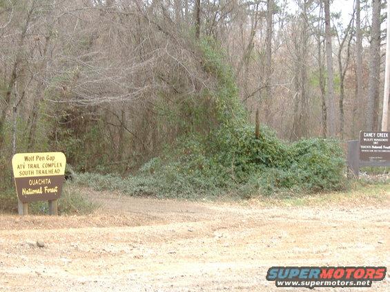 Yellow and brown trailhead signs in a wooded area with dry brush