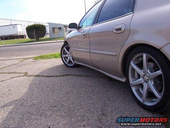 Side view of a tan sedan with custom rims parked on a cracked asphalt lot